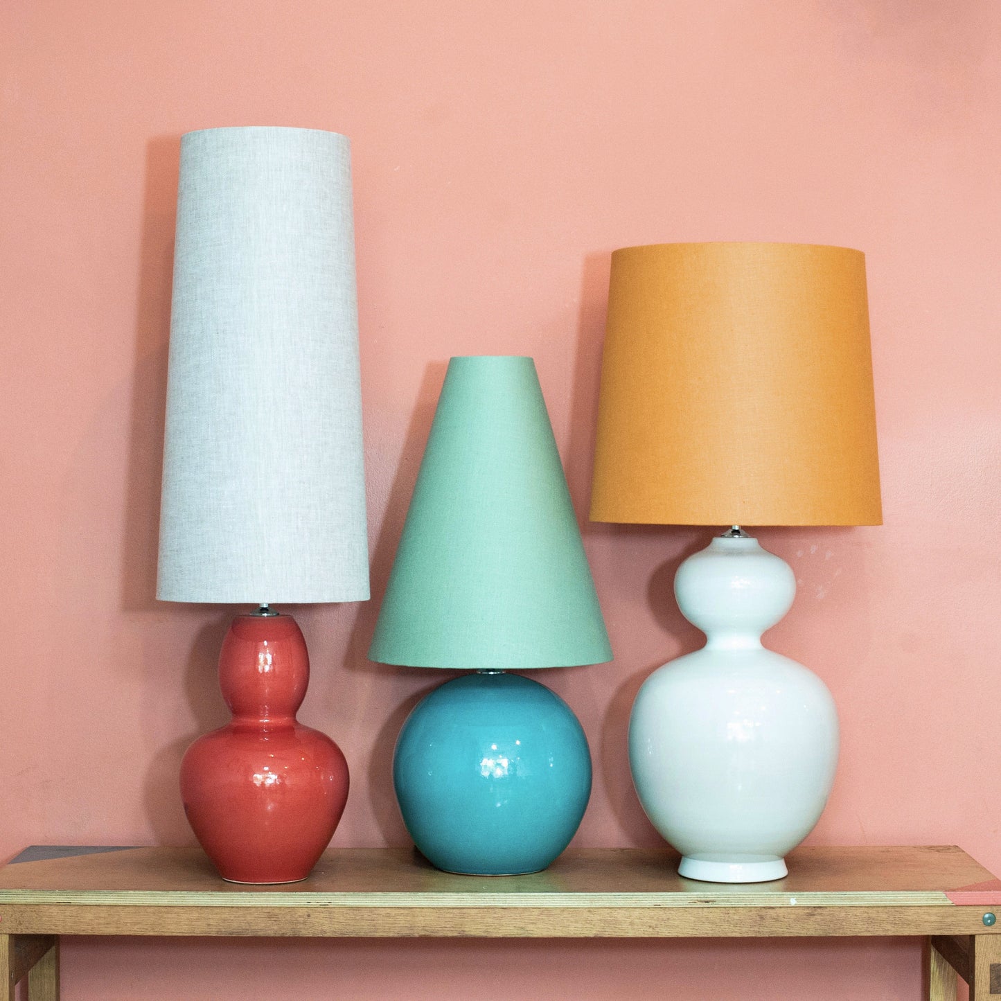A trio of colourful lamps on a wooden table against a pink wall