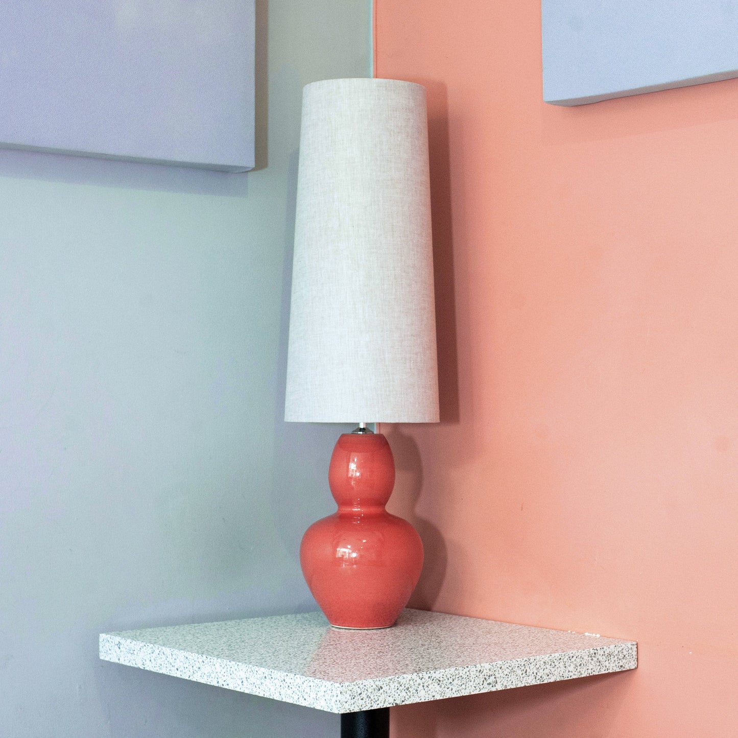 Red lamp with linen mid century lampshade on a small table against a pink wall