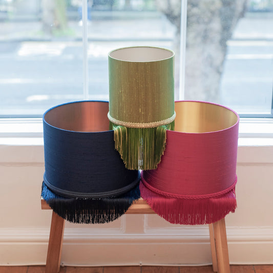 Three colorful lampshades on a wooden stool with a window in the background