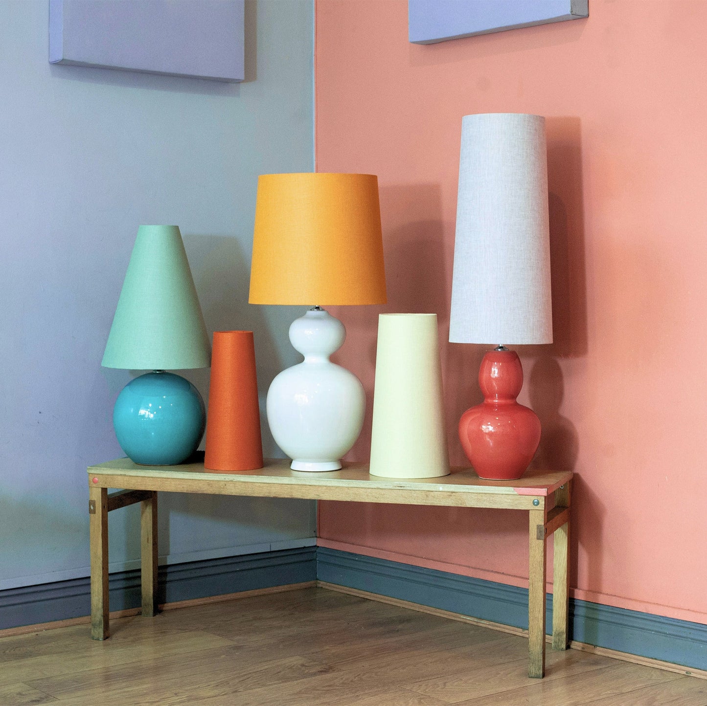 Colorful mid century style lamps and lampshades on a wooden bench against a multicolored wall.
